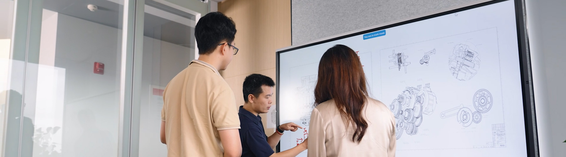 Three people standing in front of a white board looking at automotive part designs
