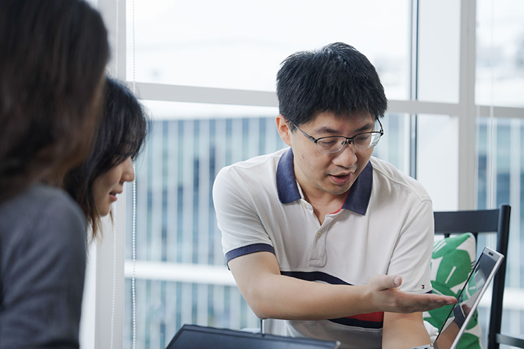 A person showing content on a laptop to two people in an office environment