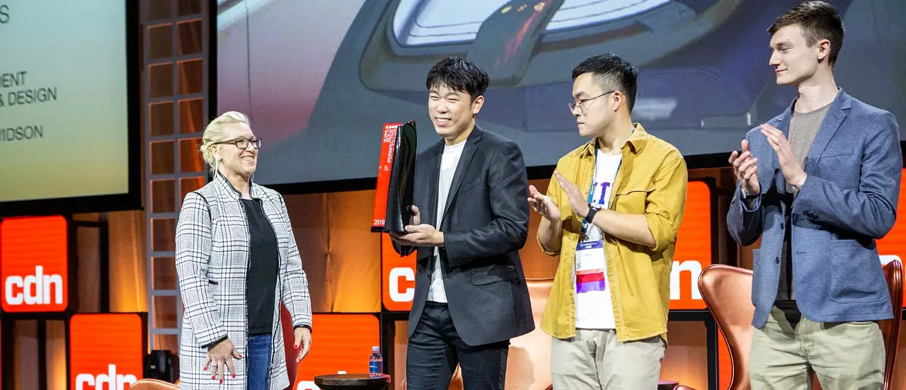 Group of people on stage during an award ceremony with one person holding a trophy