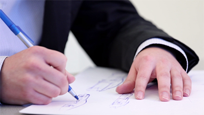 Person sketching a design on paper with a pen, wearing a business suit