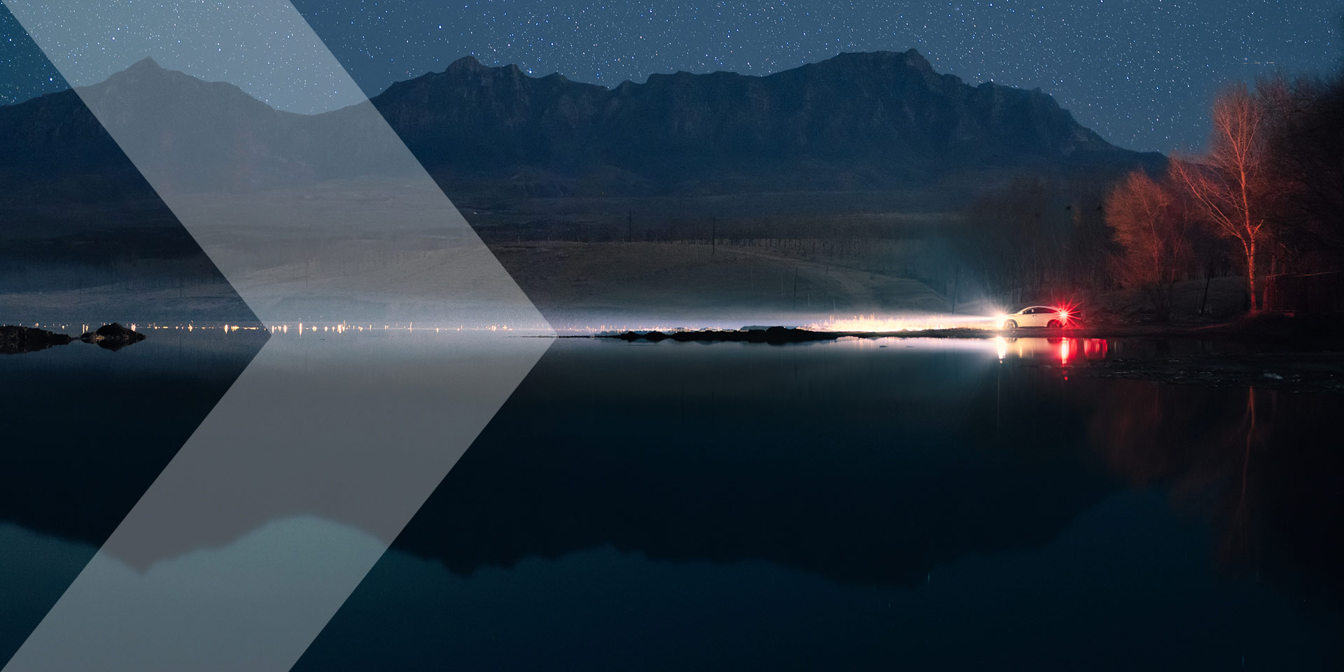 Vehicle at dusk with lights on and mountains in the background, grey chevron coming in from the left