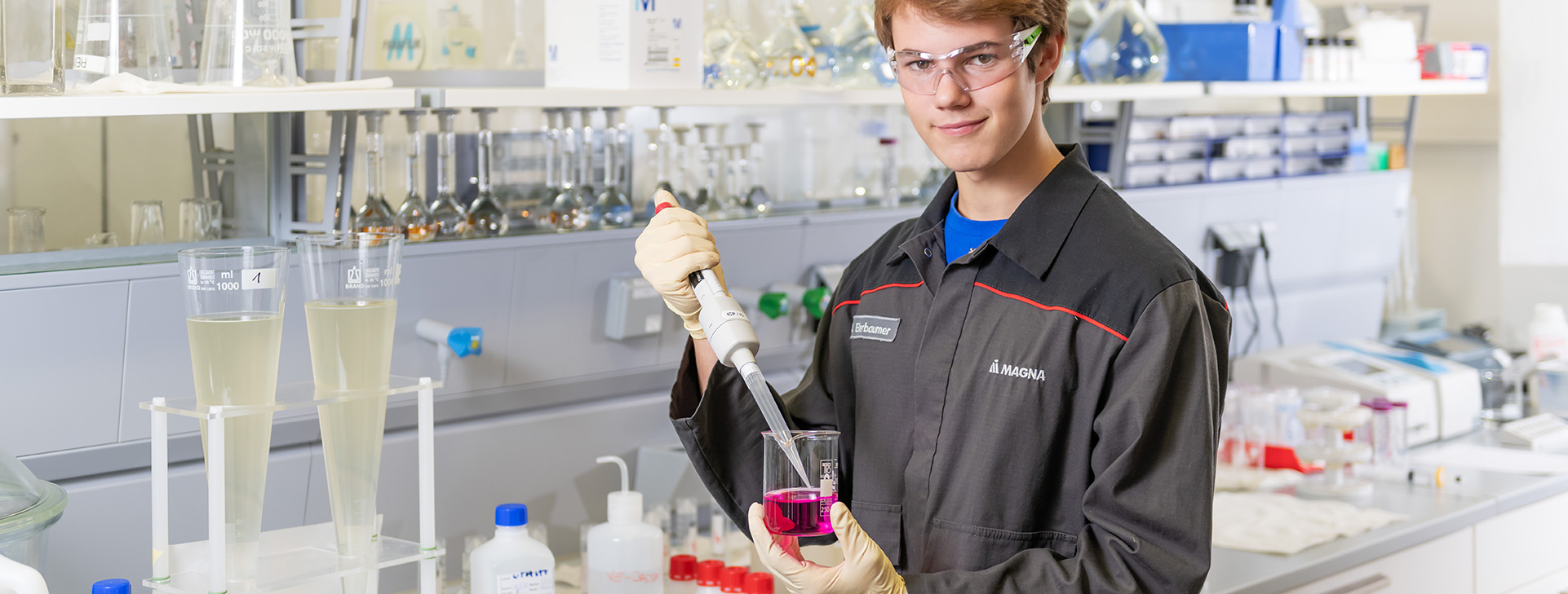 Laboratory worker using a pipette to transfer pink liquid into a beaker
