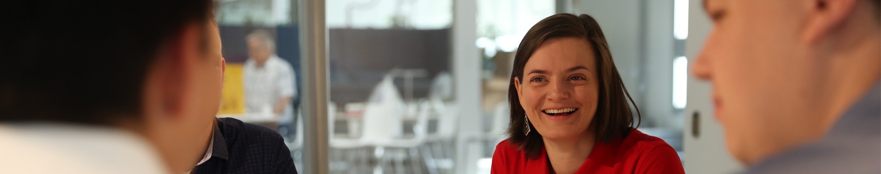 Smiling woman in a red shirt engaging in a group discussion in a modern office