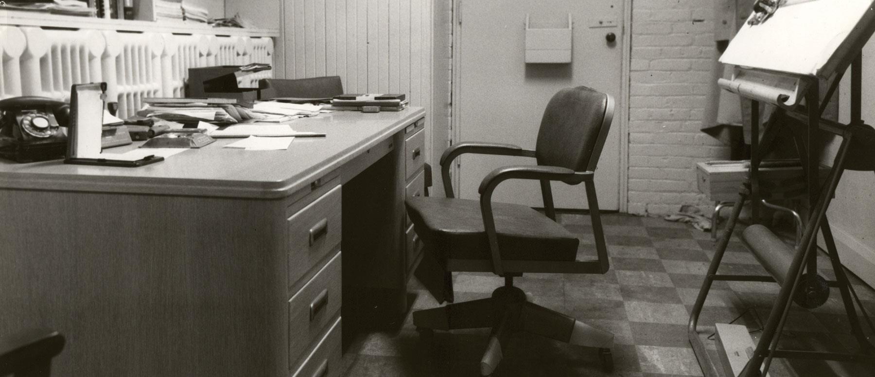 Vintage office space with a wooden desk, chair, rotary phone, and drafting table