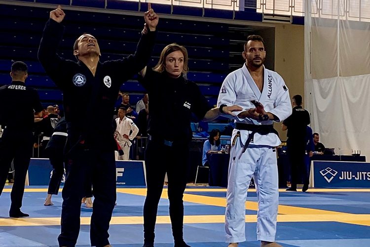 Two people and a referee at a Jiu-Jitsu match with one person being declared the winner