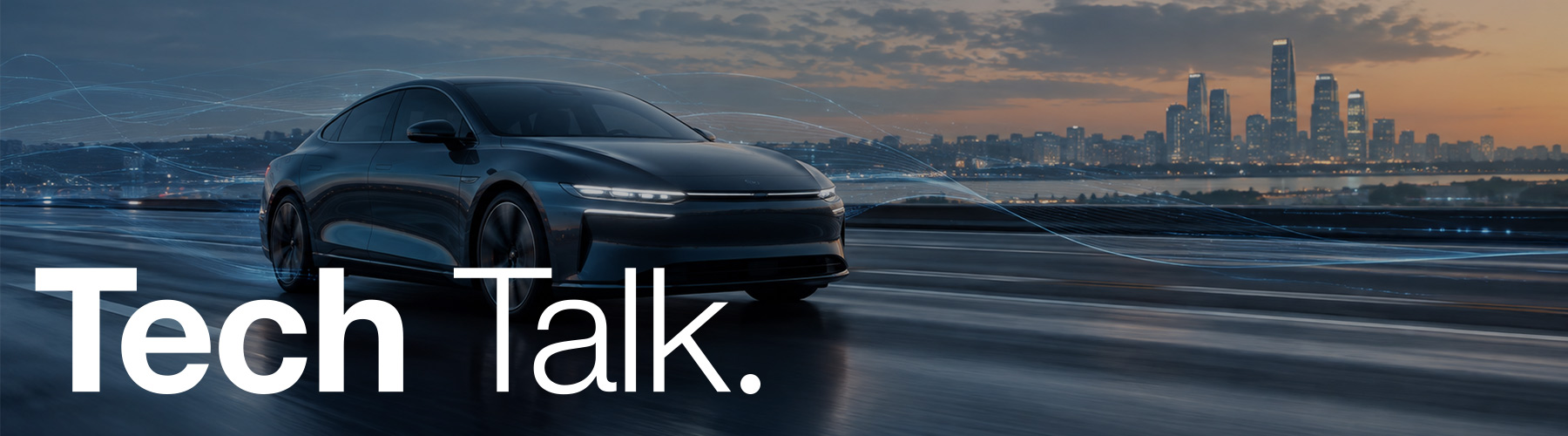Black vehicle driving along a road at dusk with the sun setting, lake and city skyline in the background. With text Tech Talk.